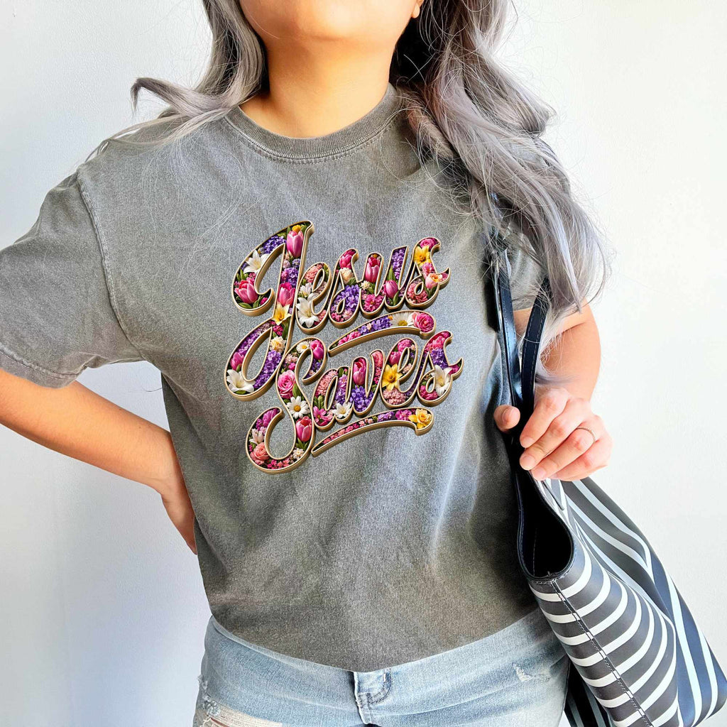 Person wearing a gray t-shirt with 'Jesus Saves' in colorful letters, holding a striped bag.