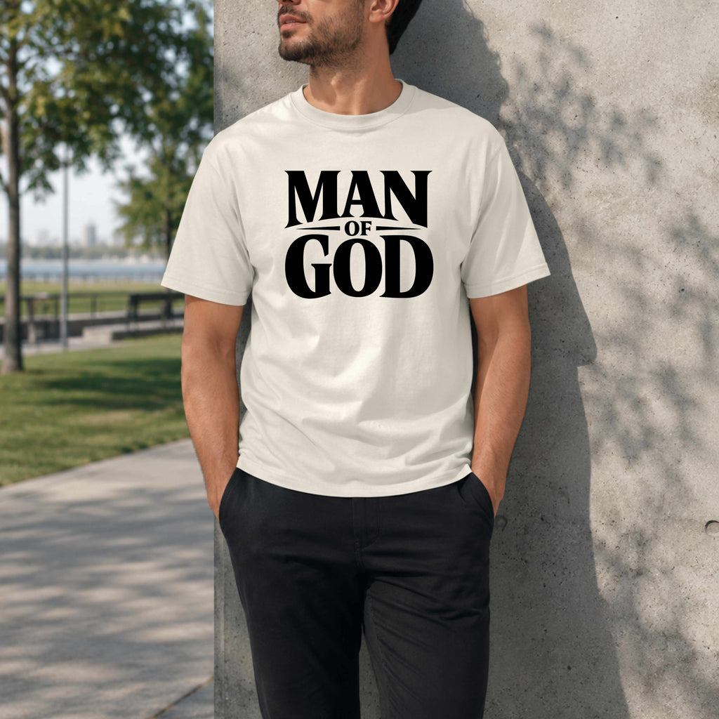 Person wearing a white t-shirt with 'Man of God' text, standing against a concrete wall outdoors.